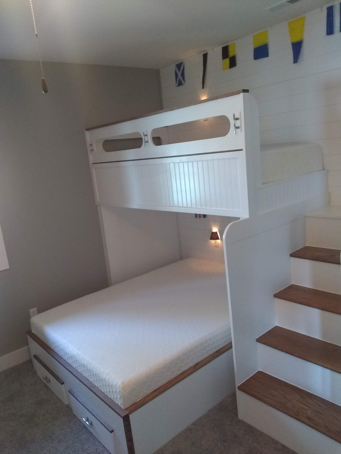 White bunk bed with wooden steps shown in a room with gray walls and a small flag decoration.